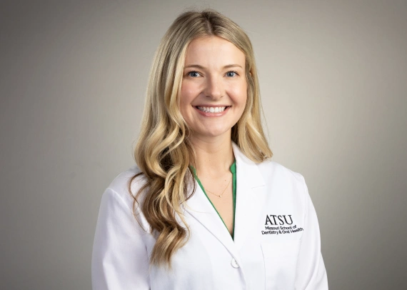 Medium shot portrait of Dr. Gracyn Lindborg smiling while wearing a white ATSU Missouri School of Dentistry lab coat.